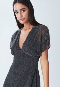 Musthave mustmustkudumis mustmustmustav mustmust with short, flowing sleeves ja sügava V-kaelusega. Läikiv kangas omab vertikaalseid rante, luues sujuva silueti.