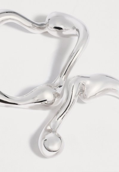 Δύο λαμπερά, αφηρημένα, κυρτά ασημένια βραχιόλια με στρογγυλεμένα άκρα σε λευκό φόντο.