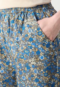 Shorts in tessuto con stampa floreale e cintura elasticizzata. Prevalentemente marroni con fiori blu e crema. Tasca laterale visibile a sinistra.