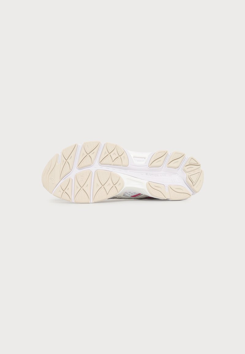 Weiße und beige Laufschuhsohle mit geometrischen Gripmustern auf einfachem hellgrauem Hintergrund.