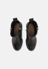 Botines de cuero negro con textura suave, puntera redondeada, dos tiradores y acentos metálicos en el lateral. Diseño de suela plana.