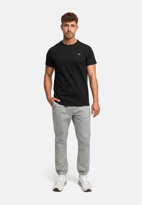 Black cotton t-shirt with short sleeves and a crew neck, paired with light gray pants and white sneakers. Minimalist design with no patterns.