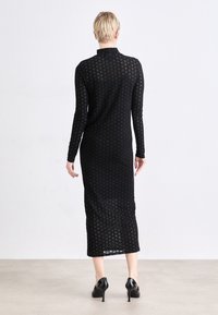 Black long-sleeve dress made of textured knit fabric with a fitted silhouette and mid-calf length, featuring a high neckline and subtle pattern.