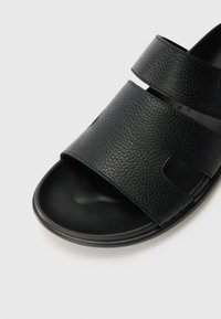 Black leather sandal featuring two wide adjustable straps, textured surface, open toe design, and a smooth black sole.