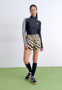 Μαύρη μπλούζα με μακριά μανίκια και λευκές ρίγες, κίτρινα σορτς με μαύρο ζευγάρι ζέβρας, μαύρες κάλτσες μέχρι το γόνατο και μαύρα sneakers με λευκές ρίγες.