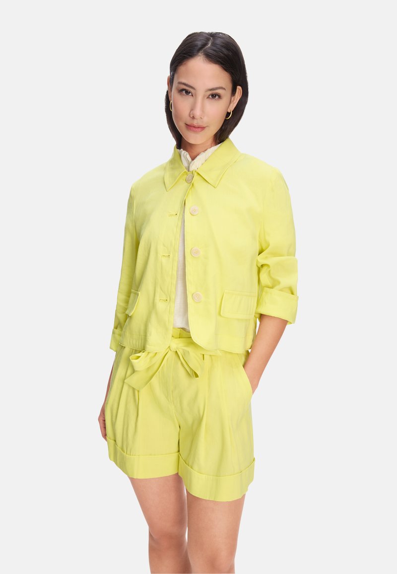 Yellow linen jacket with a collar, front buttons, and two pockets, paired with matching shorts featuring a tie waist and rolled hems.