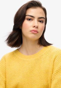 Geel gebreid sweater met een gestructureerd patroon en een brede ronde halslijn, met ribbelaccenten bij de manchetten en de zoom.