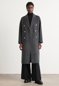 Dubbele-breasted jas in een grijze houndstooth print, met gouden accenten, een geknipte kraag en een rechte snit. Draag hem over een zwarte coltrui.