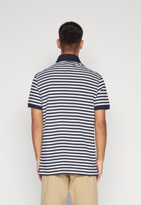 Polo in cotone a righe navy e bianche, con colletto classico e maniche corte; presenta un orlo dritto e spacco laterale.