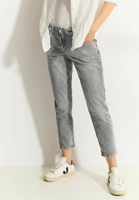 Pantalon court rayé gris et blanc à coupe décontractée, avec une ceinture boutonnée et des poches latérales, associé à des baskets blanches.