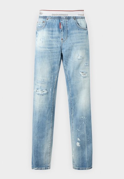 Ανοιχτό μπλε τζιν με φθορές, ξεθωριασμένες κηλίδες και σκισίματα, εμφανιζόμενο με λευκή ελαστική μέση με λογότυπο που είναι ορατή πάνω από το τζιν.