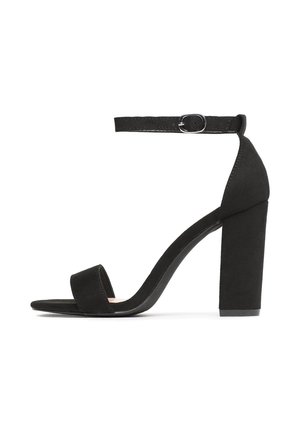 Sandale à talon haut en daim noir avec une large bride à l'avant du pied, une boucle à la cheville et un talon épais. Texture lisse et design ouvert à l'arrière.