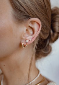 Orecchini in oro con design floreali e geometrici, arricchiti da piccole pietre trasparenti, che mettono in risalto dettagli intricati e texture variate.