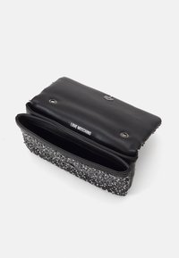 Svart skinnclutch med et sølvfarget paljettmønster på den nedre halvdelen, med trykknapplås og et innvendig rom.