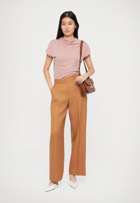 Haut rose clair à col bénitier, pantalon marron taille haute et pattes larges, escarpins blancs à bout pointu et un petit sac à épaule marron.