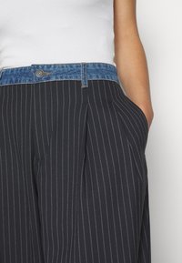 Námořnické kalhoty s proužkem a denímovým pasem, s předními sklady a bočními kapsami. Materiál vypadá měkce s viditelnými švy.