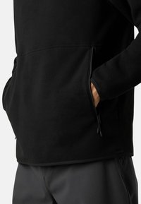 Czarny polarowy półgolf o gładkiej fakturze, z zamykanymi bocznymi kieszeniami i kontrastowym wykończeniem na dole i rękawach. Prosty, funkcjonalny design.