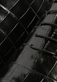 Zapato de cuero negro con un acabado brillante, que presenta un patrón texturizado de cocodrilo y cordones negros a lo largo del costado.