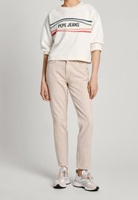 Bílá mikina se znakem "PEPE JEANS" a barevnými pruhy. Světle béžové kalhoty, přiléhavý design. Šedé a bílé sneakers se šněrováním.