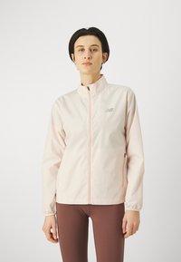 Giacca a vento rosa chiaro con colletto alto, logo argento, chiusura con zip e polsini elasticizzati. Texture liscia e design aderente.
