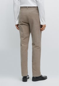 Pantaloni in corduroy beige con una vestibilità dritta, caratterizzati da due tasche posteriori e una texture liscia, abbinati a mocassini neri.
