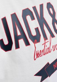 Biała bawełniana koszulka z nadrukiem w odważnym, ciemnoniebieskim i czerwonym kolorze z napisami "JACK&" oraz "Essential wear", ozdobiona motywem w kształcie banera.