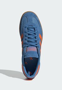 Blue suede sneaker with orange stripes, textured mesh upper, and a patterned insole. Features traditional laces and a gum rubber sole.