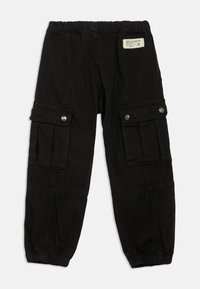 Calças cargo pretas com um cordão na cintura, múltiplos bolsos laterais e punhos elásticos. Feitas de um tecido durável e texturizado. Etiqueta nas costas.