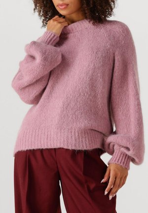 Roze pluizige trui met een geribbelde halslijn en manchetten. Ronde vorm met volumineuze mouwen en een losse pasvorm, gecombineerd met bordeauxrode broeken.