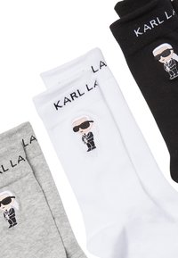 Fehér, szürke és fekete zoknik, rajzfilmfigurás mintával, napszemüveggel és öltönyben. A "KARL LAGERFELD" logó minden zokni szárán.