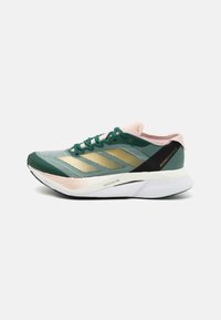 Zielony i czarny but do biegania z siatkową cholewką, złotymi paskami i różowymi akcentami. Posiada lekką podeszwę oznaczoną napisem "LIGHTSTRIKE PRO".