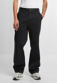 Black cotton trousers with a straight leg fit, featuring side pockets, a button closure, and a smooth texture. Worn with grey sneakers.