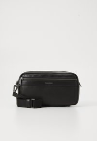 Black leather crossbody bag with a zippered compartment, textured surface, adjustable strap, and Calvin Klein branding on the front.