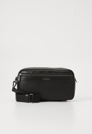 Zwarte leren schoudertas met een ritsvak, gestructureerd oppervlak, verstelbare schouderband en Calvin Klein-logo op de voorkant.