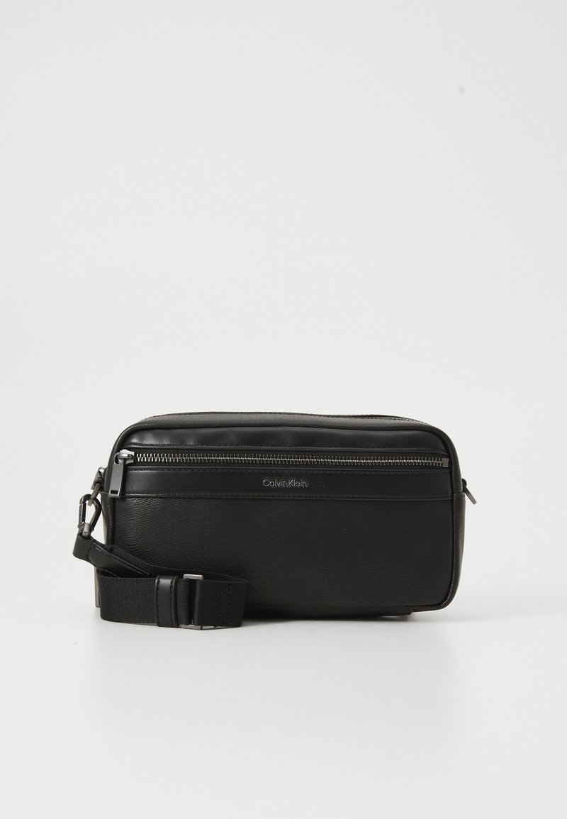 Black leather crossbody bag with a zippered compartment, textured surface, adjustable strap, and Calvin Klein branding on the front.