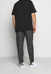 Svart t-shirt, lös passform. Grå rutiga byxor med ljusa linjer, avslappnad form. Vita sneakers med gröna detaljer, platta sulor. Enkelt design.