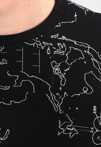 Felpa nera con stampa bianca a contorno simile a una mappa, dotata di scollatura a costine e tessuto testurizzato. Il design include dettagli geografici e linee.