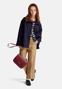 Námořnická bunda, pruhovaný svetr, béžové kalhoty a bordeaux texturovaná kabelka s popruhem. Černé mokasíny dokončují outfit.