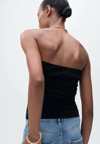 Top a tubino nero a costine con un design aderente, abbinato a pantaloni corti di jeans blu a vita alta. Texture liscia e stile minimalista.
