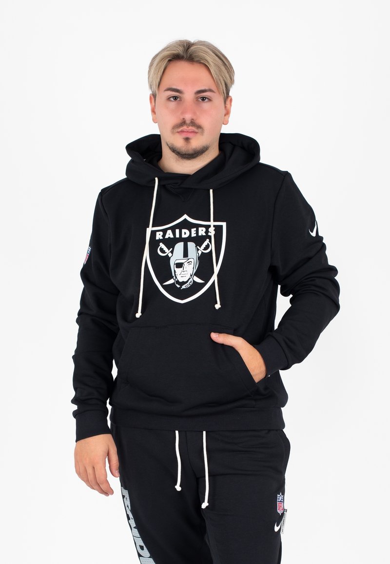 Zwarte hoodie met een Raiders-logo op de voorkant en witte trekkoorden. Voorzien van een kangoeroezak en geribde manchetten, gecombineerd met zwarte broek.