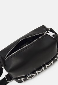 Czarna skórzana torba na ramię z srebnym zamkiem, z wyraźnym logo "TOMMY" na pasku oraz eleganckim prostokątnym kształtem.