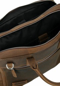 Bolso mensajero de cuero marrón con dos compartimentos con cremallera y interior de tela oscura. Incluye detalles de herrajes y asas resistentes.