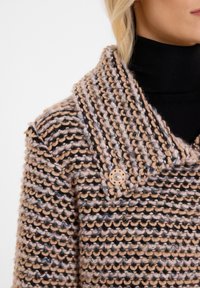 Strickmantel mit weitem Kragen, gestreiftem Muster in Beige, Braun und Schwarz sowie einem dekorativen Knopf am Kragen. Texturierter Stoff.