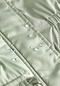 Material rezistent la apă, de culoare verde deschis, cu o textură netedă, având picături pe suprafață și detalii vizibile de cusătură.