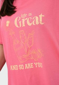 Różowa bawełniana koszulka z żółtym nadrukiem przedstawiającym butelkę szampana, dwa kieliszki i truskawki, z tekstem "Życie jest wspaniałe" i "I TY TEŻ".