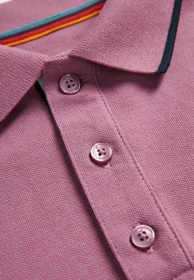 Kortærmet polo shirt i lys lilla tekstureret stof. Har en ribbet krave med teal, rød og sort striber samt tre lyserøde knapper.