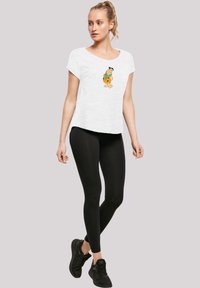 Weißes Kurzarm-T-Shirt mit einem Cartoon-Charakter-Druck auf der Vorderseite, kombiniert mit schwarzen Leggings und schwarzen Turnschuhen.