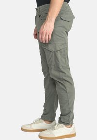 Khaki cargobroek met een tapse pasvorm, zijzakken en achterzakken; vervaardigd van zacht katoen met gestikte details. Gekocht met witte sneakers.