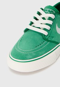 Zelene suede tenisice s bijelim vezicama, šivanim detaljima i gumenenim potplatom koji ima teksturirani riblji uzorak. Vidljiv srebrni logo.