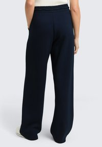 Hose mit weit geschnittenem Bein aus dunkelblauem Stoff und elastischem Bund, ausgestattet mit Taschen an den Seiten und einer glatten Textur.